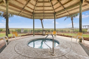 A covered outdoor swimming pool with a wooden roof, surrounded by benches and a fenced area.