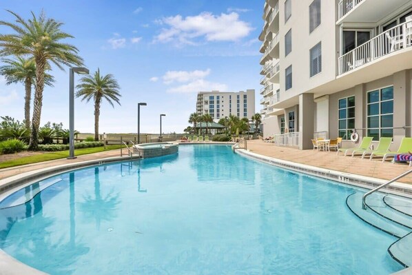 A swimming pool with lounge chairs and palm trees, surrounded by a building with balconies.