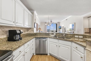 A modern kitchen with white cabinetry, granite countertops, a dishwasher, and a coffee maker.