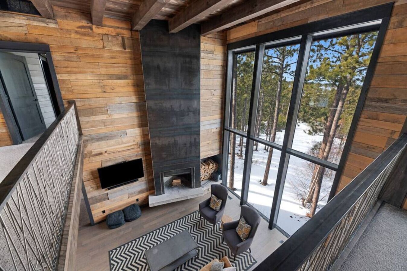 Ein modernes Interieur mit Kamin, Holzwänden und großen Fenstern mit Blick ins Freie.