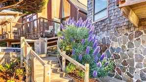 Eine Holztreppe führt zu einem Haus mit einer Steinmauer und einem Garten voller violetter Blumen.