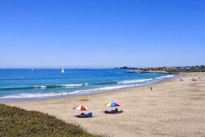 Une plage avec un ciel dégagé, un rivage sablonneux et quelques parasols.