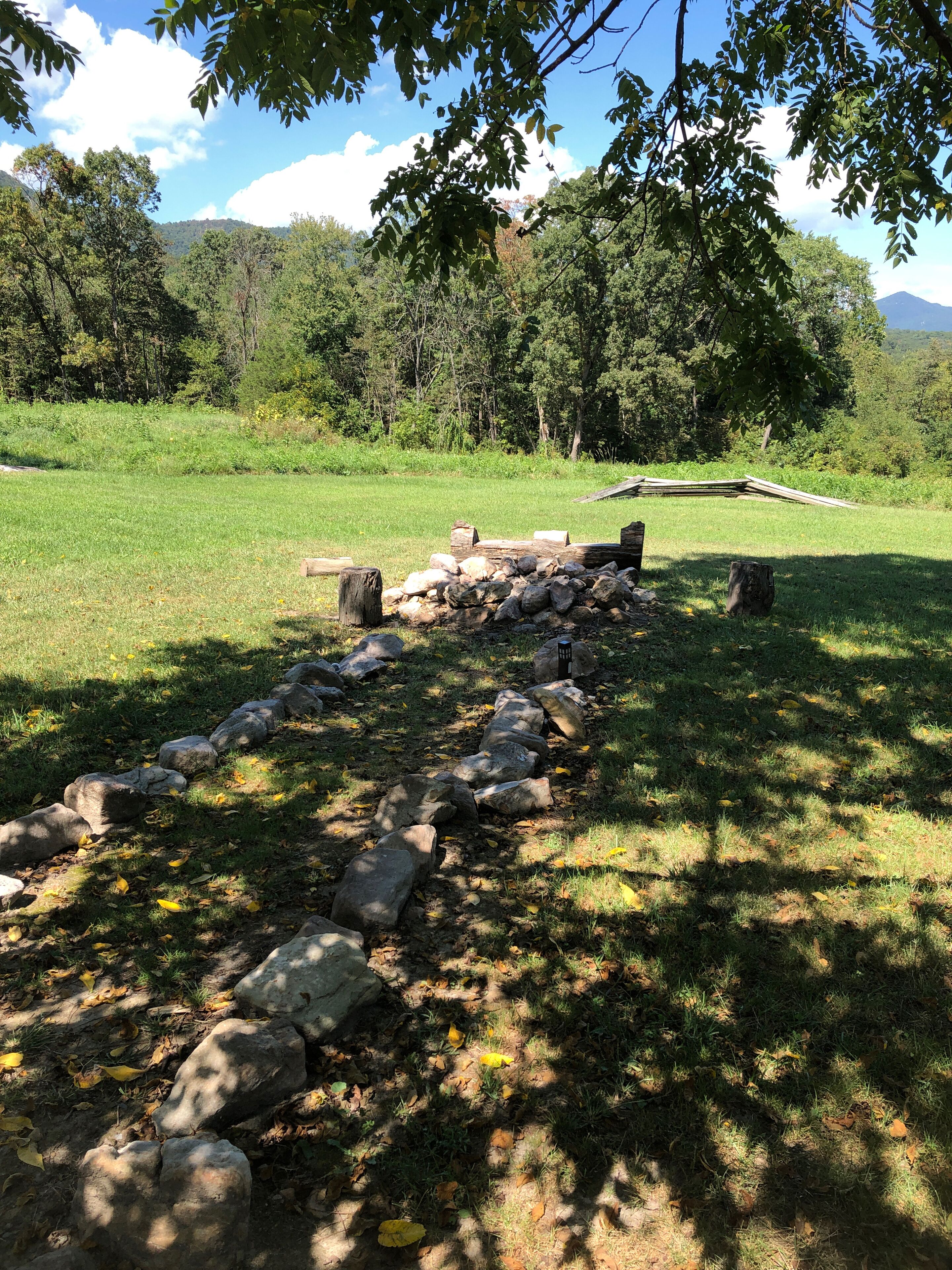 A stone pathway leading through a grassy field with trees and a mountain in the background.