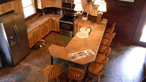 Une cuisine dotée de meubles en bois, d’un réfrigérateur, d’un four, d’une cuisinière, d’un évier et d’un coin bar avec des tabourets.