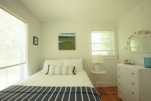 Ein Schlafzimmer mit einem Bett, einem Fenster, einer Kommode und einem Bild an der Wand.
