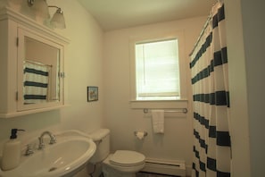Ein Badezimmer mit weißem Waschbecken, Toilette und einem Fenster mit Jalousien.