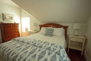 Une chambre à coucher avec un lit, une commode, une table de chevet et une lampe.