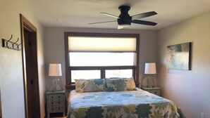 A bedroom with a bed, two bedside tables, a ceiling fan, a window with blinds, and a colorful rug. - Your Basecamp In the Tetons.  (Victor)
