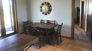 A dining area with a wooden table and chairs, a wall clock, and a view through an open door. - Your Basecamp In the Tetons.  (Victor)