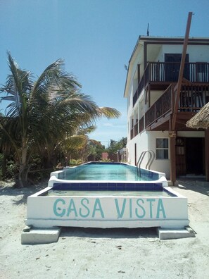 Una piscina con el rótulo 'GASA VISTA' en una playa arenosa con un edificio al fondo.