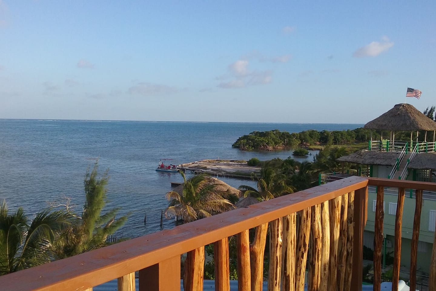 A coastal view with a wooden deck railing, a thatched-roof structure, and a flag on a pole.