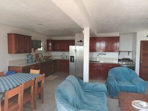 A compact kitchen with wooden cabinets, a refrigerator, a stove, and a dining area with a table and chairs.