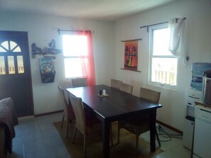 Un coin repas avec une table et des chaises en bois, un distributeur d’eau et une fenêtre avec des rideaux.