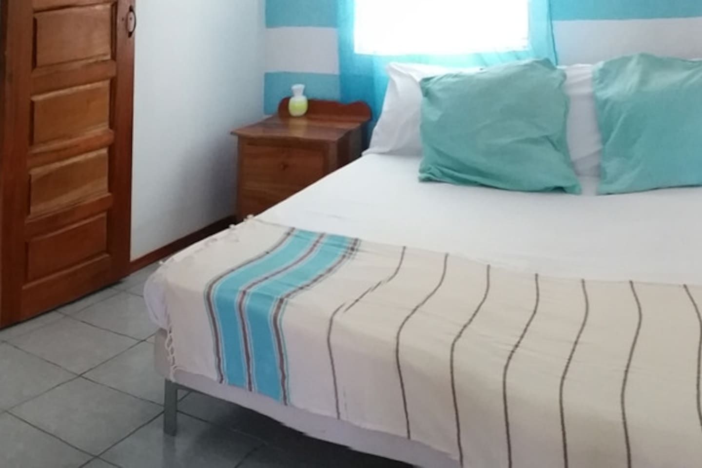 A bedroom with a bed, a wooden wardrobe, a nightstand, and a window with curtains.