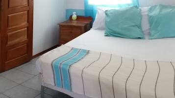A bedroom with a bed, a wooden wardrobe, a nightstand, and a window with curtains.