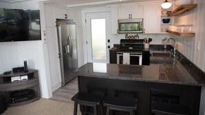 A modern kitchen with a large island, stainless steel appliances, and a flat-screen TV mounted on the wall. - RENT YOUR OWN ISLAND on beautiful Lake Winnipesaukee! (Laconia)