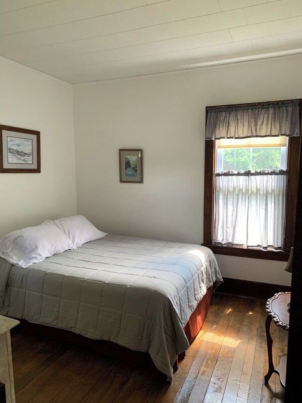A small, simple bedroom with a single bed, a window with curtains, and two framed pictures on the wall.