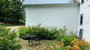 Een wit huis met een pad van stenen dat leidt naar een klein terras met een tafel en stoelen.