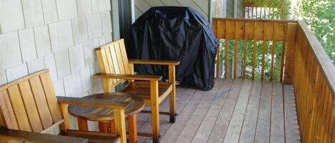 Una terrassa de fusta amb dues cadires de fusta i un parell de barbacoa coberta.