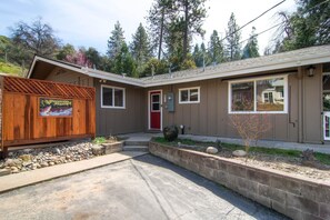 Une maison de plain-pied avec une porte rouge, un petit jardin devant, délimité par une clôture en bois, et une enseigne.