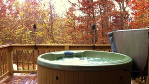A hot tub on a wooden deck with a view of autumn trees.