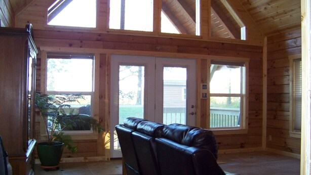 A log cabin interior with a leather sofa, a potted plant, and a view through large windows.