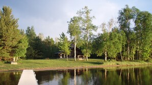 Une jetée en bois s’avançant dans un lac paisible, entourée d’une végétation luxuriante et d’une petite cabane.