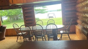 L’intérieur d’un chalet en bois comprend une table et des chaises, une fenêtre donnant sur une zone herbeuse et, à l’extérieur, une balançoire.