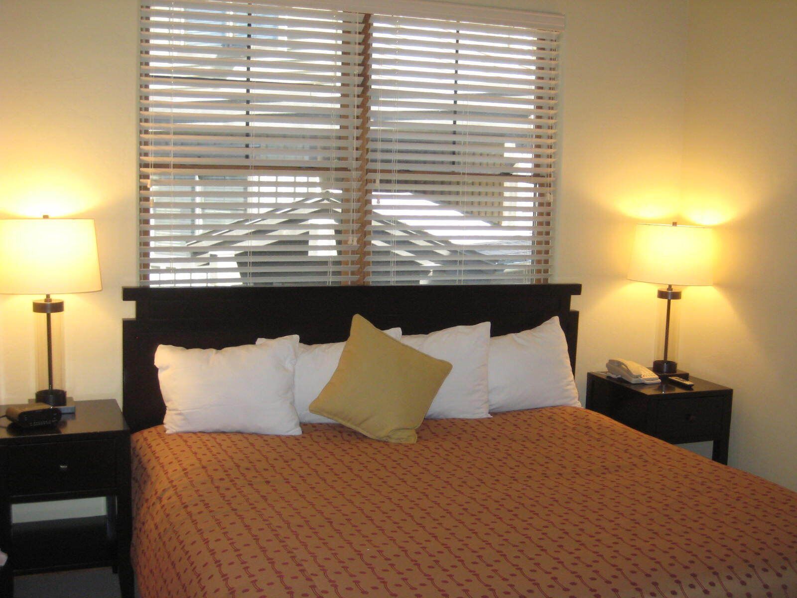 A hotel room with a bed, two bedside tables, a telephone, and a window with blinds.
