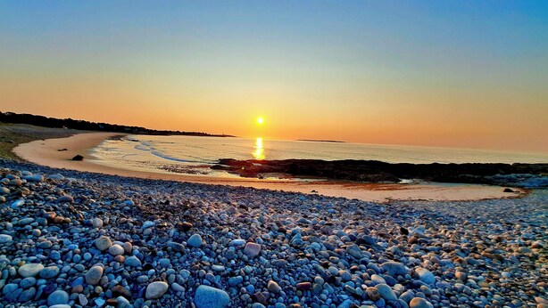 Una playa de guijarros con un atardecer sobre el océano.