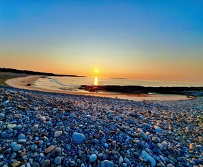 A pebbled beach with a sunset over the ocean.
