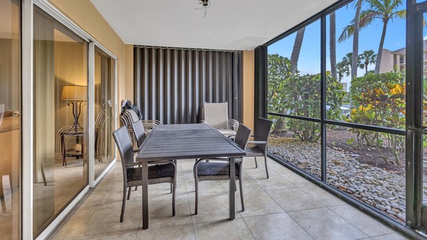 Un espace repas comprenant une table et des chaises, une porte-fenêtre coulissante et une vue sur des palmiers et des immeubles.