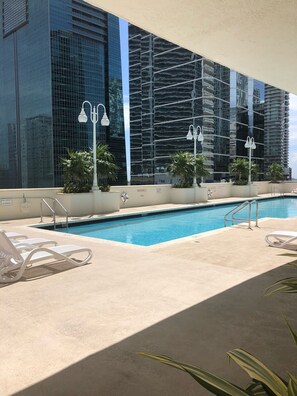 Una piscina con sillas de descanso, rodeada de edificios con fachadas de vidrio reflectante.