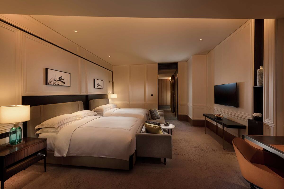 A hotel room with two beds, a TV, a desk, and a small table.