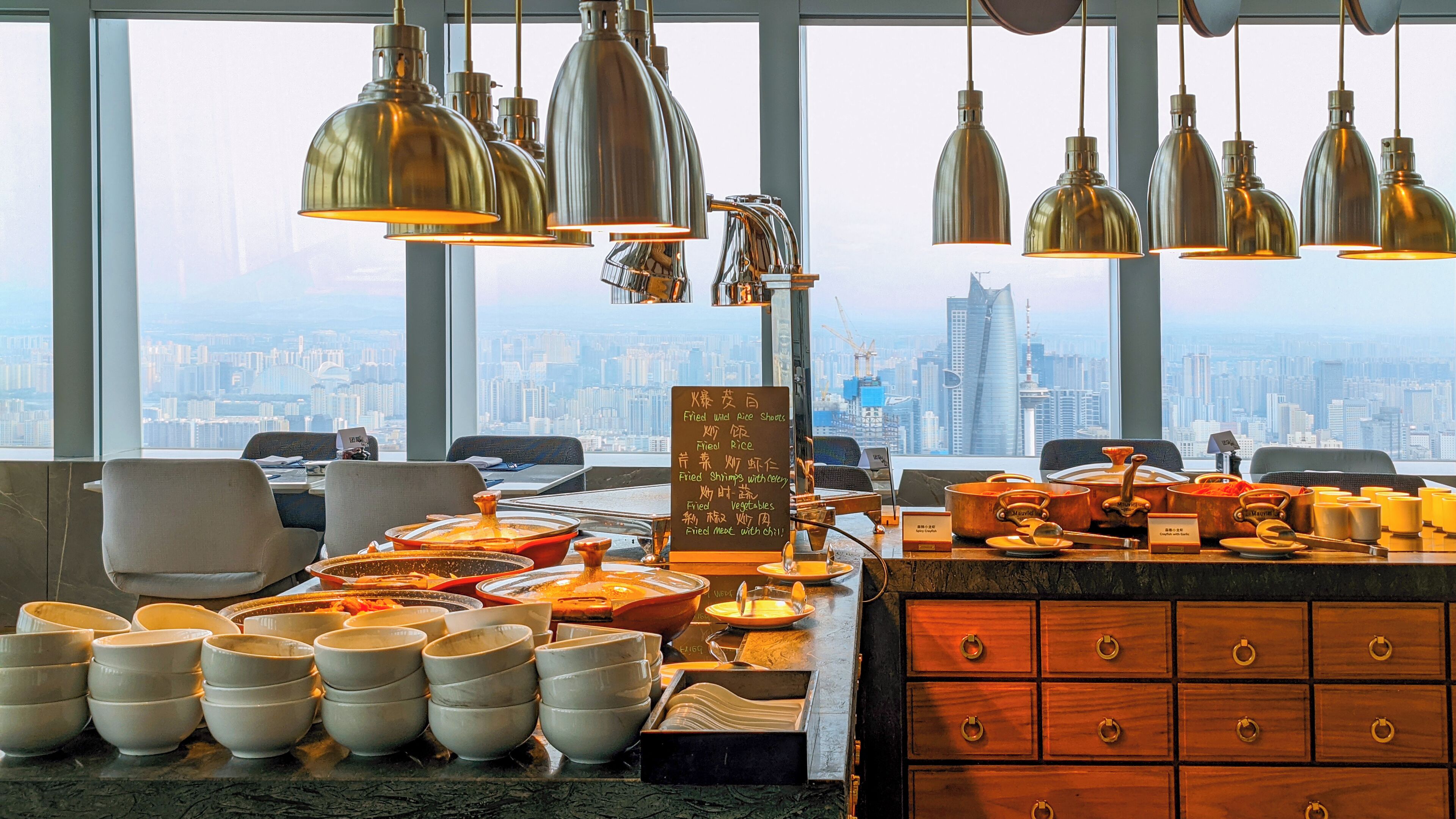 A dining area with a city view, multiple dining tables, and a variety of dishes displayed.