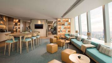 A modern hotel lobby with a bar, seating area, and large windows offering a city view.