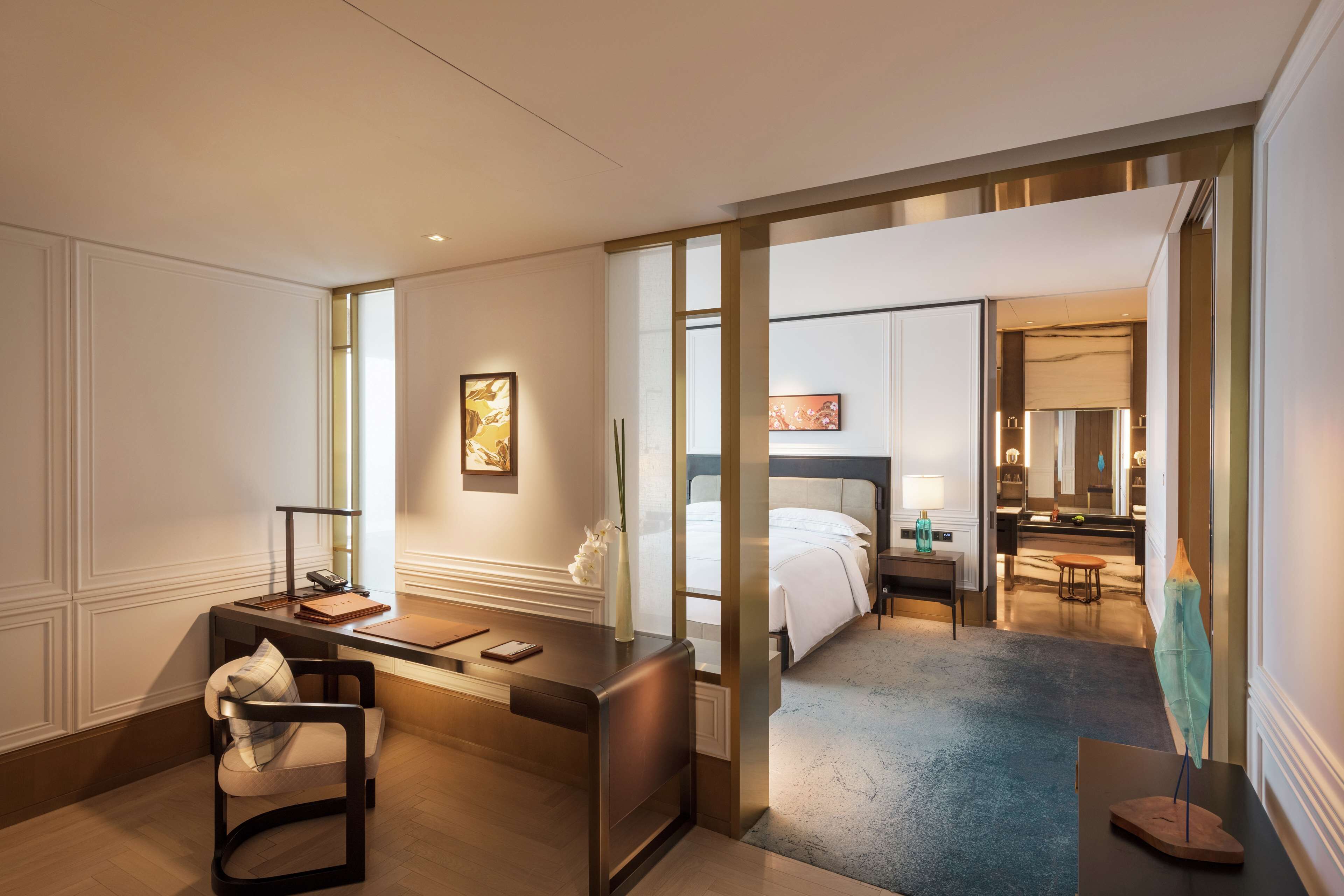 A hotel room with a desk, chair, bed, and a bathroom visible through an open door.