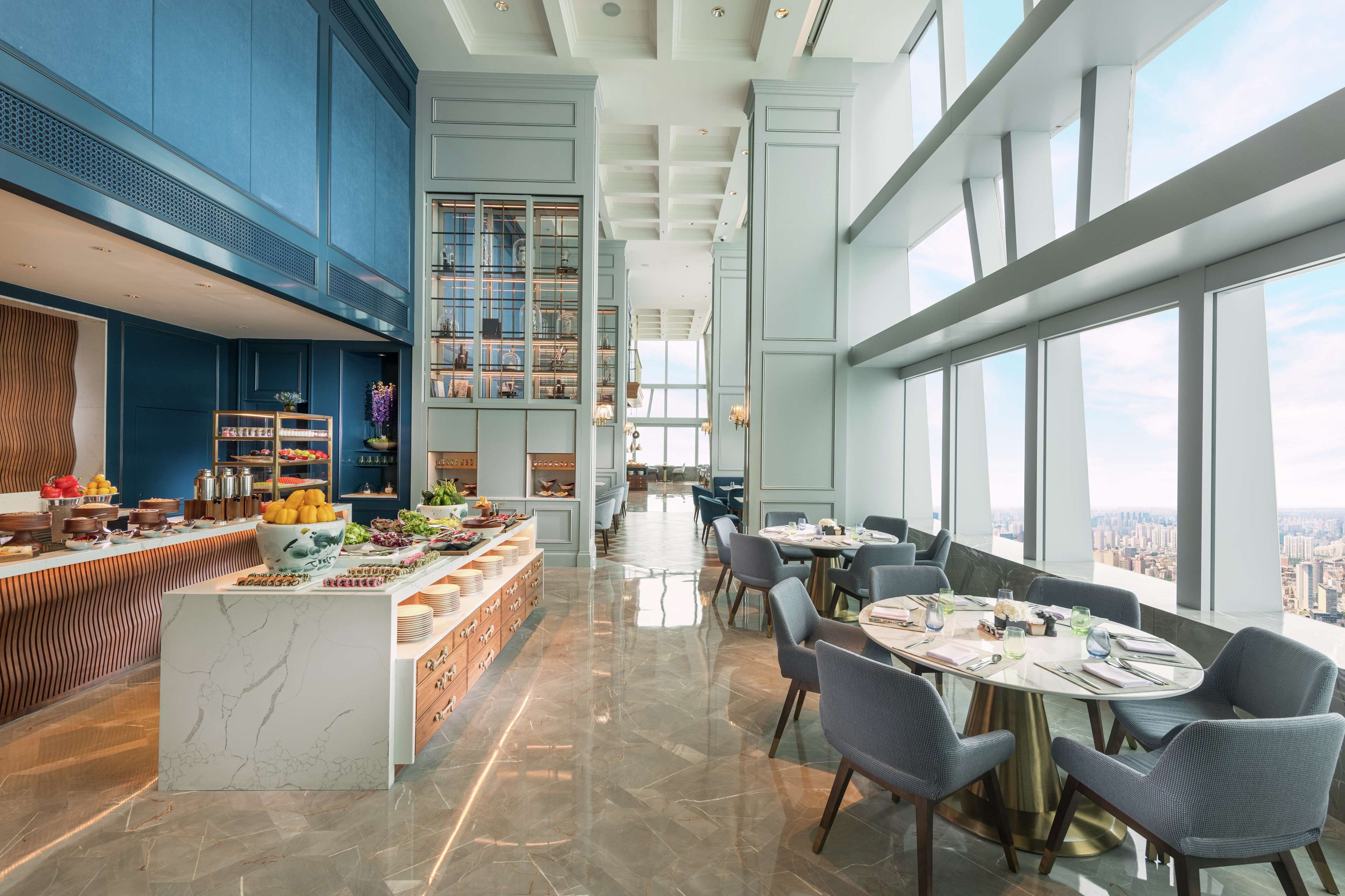A modern dining area with a long counter, seating, and a city view.