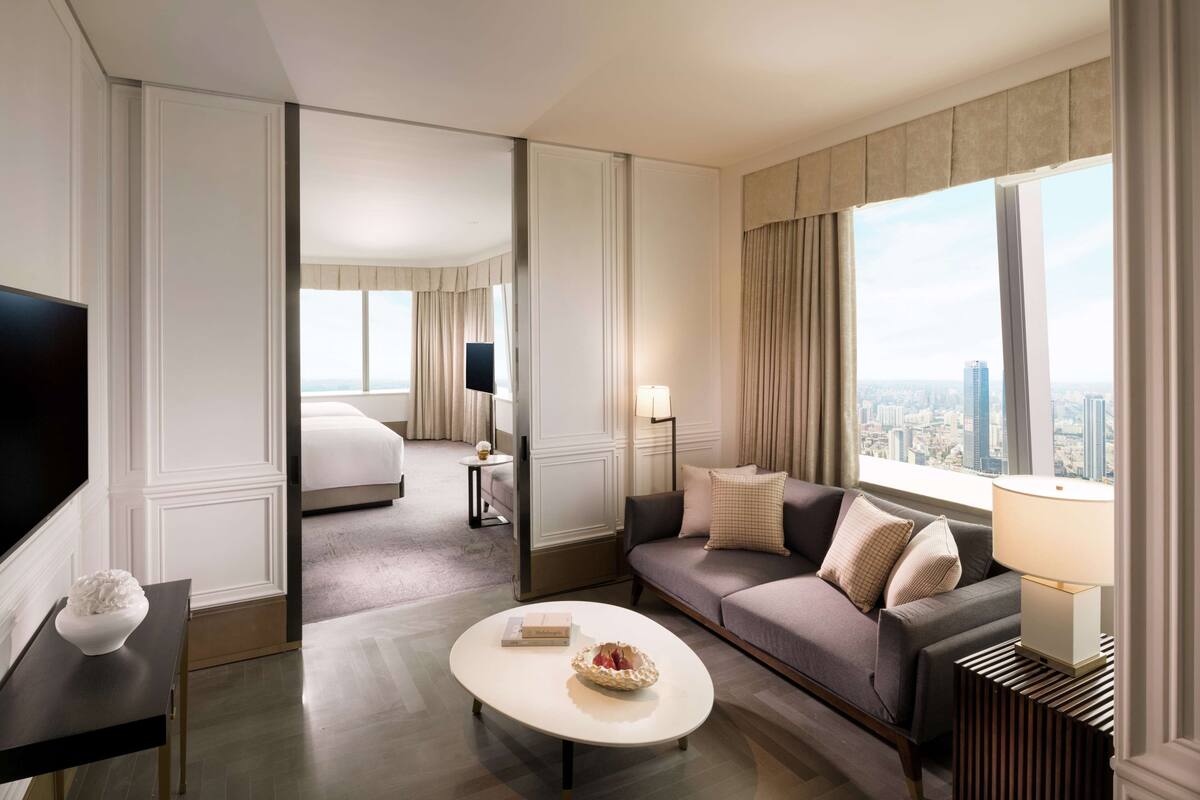A modern hotel room with a large bed, a sofa, a coffee table, and a TV.