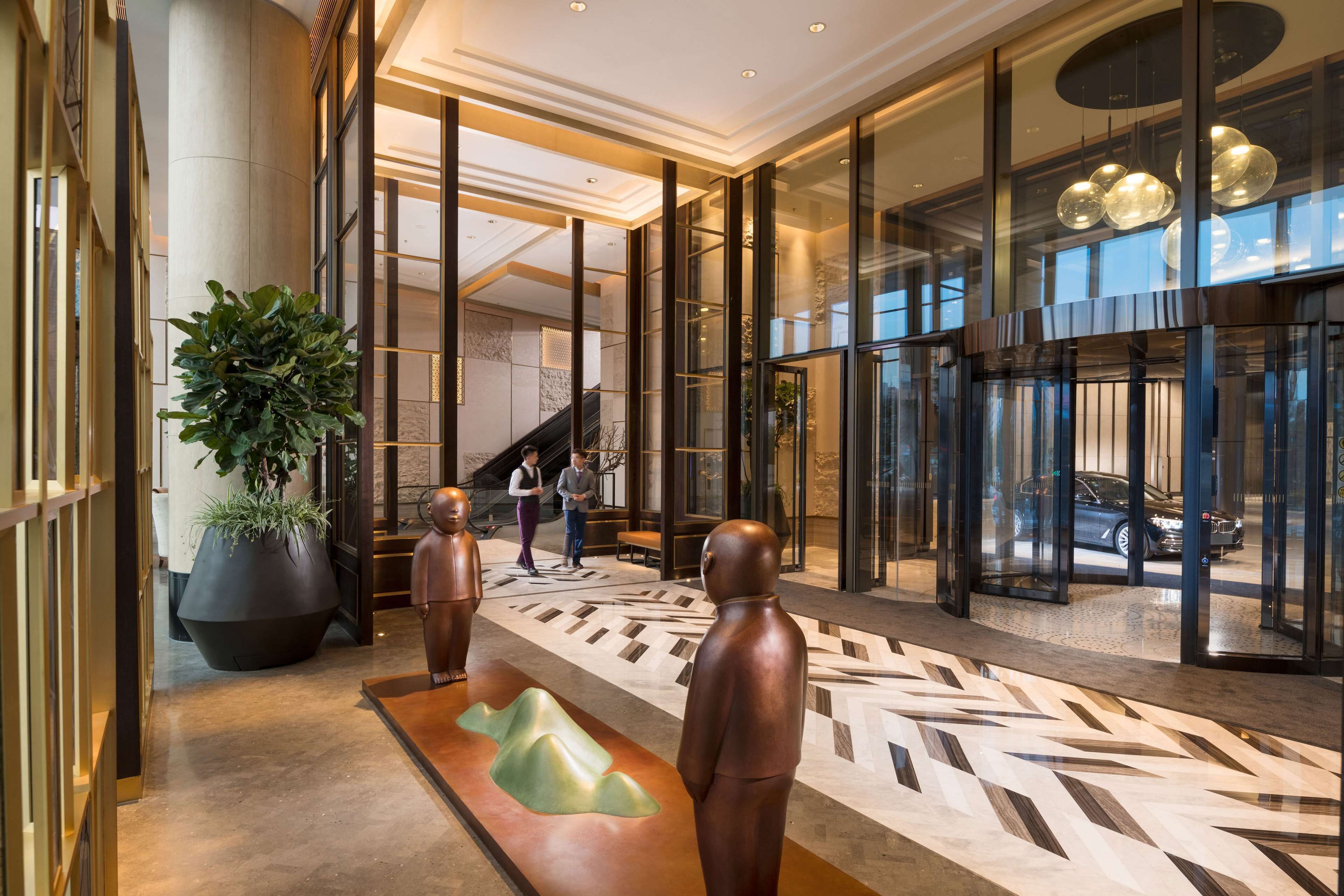 A modern lobby with glass doors, a large potted plant, and a reception desk.