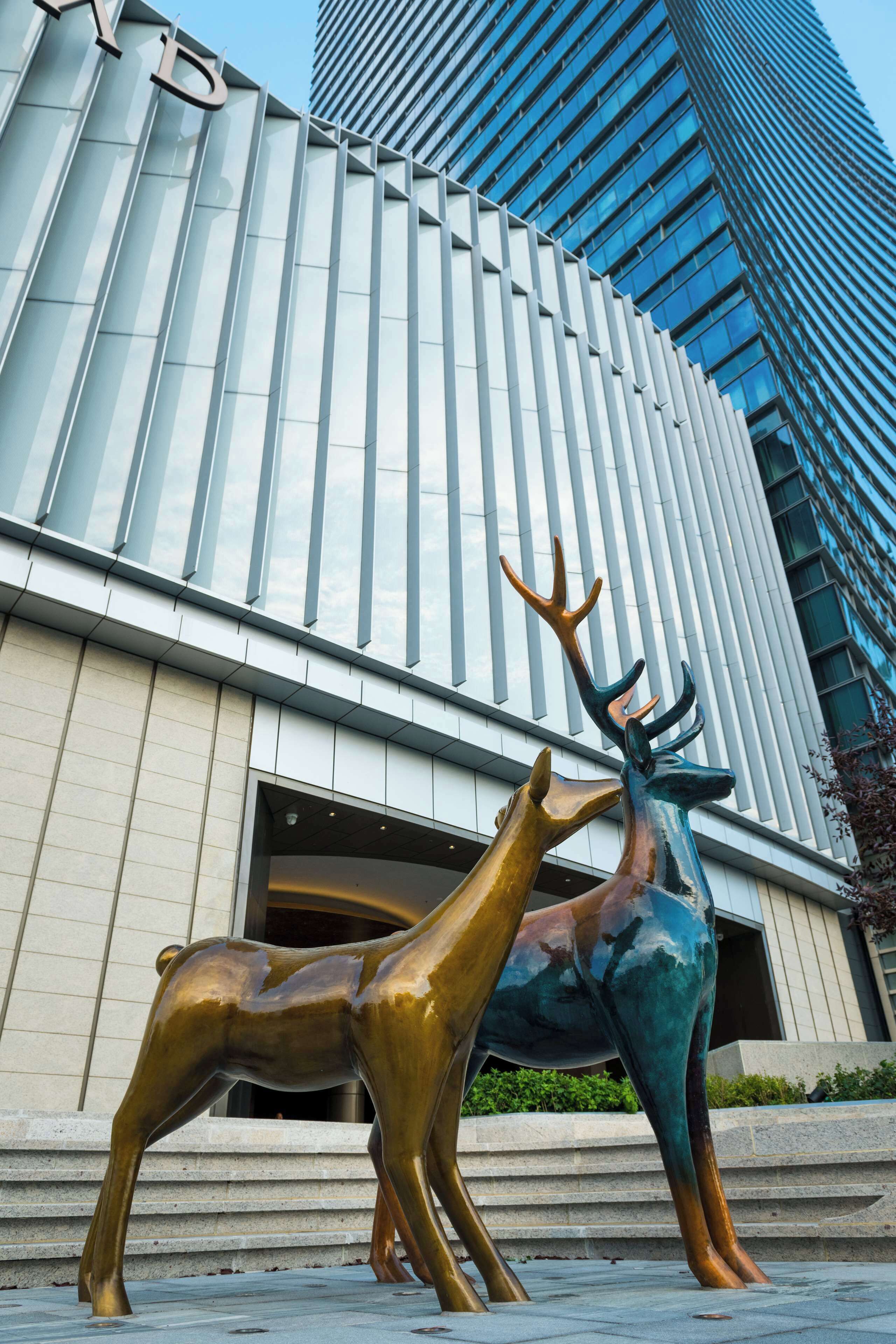 A modern building with a unique facade and a sculpture of two deer in front.
