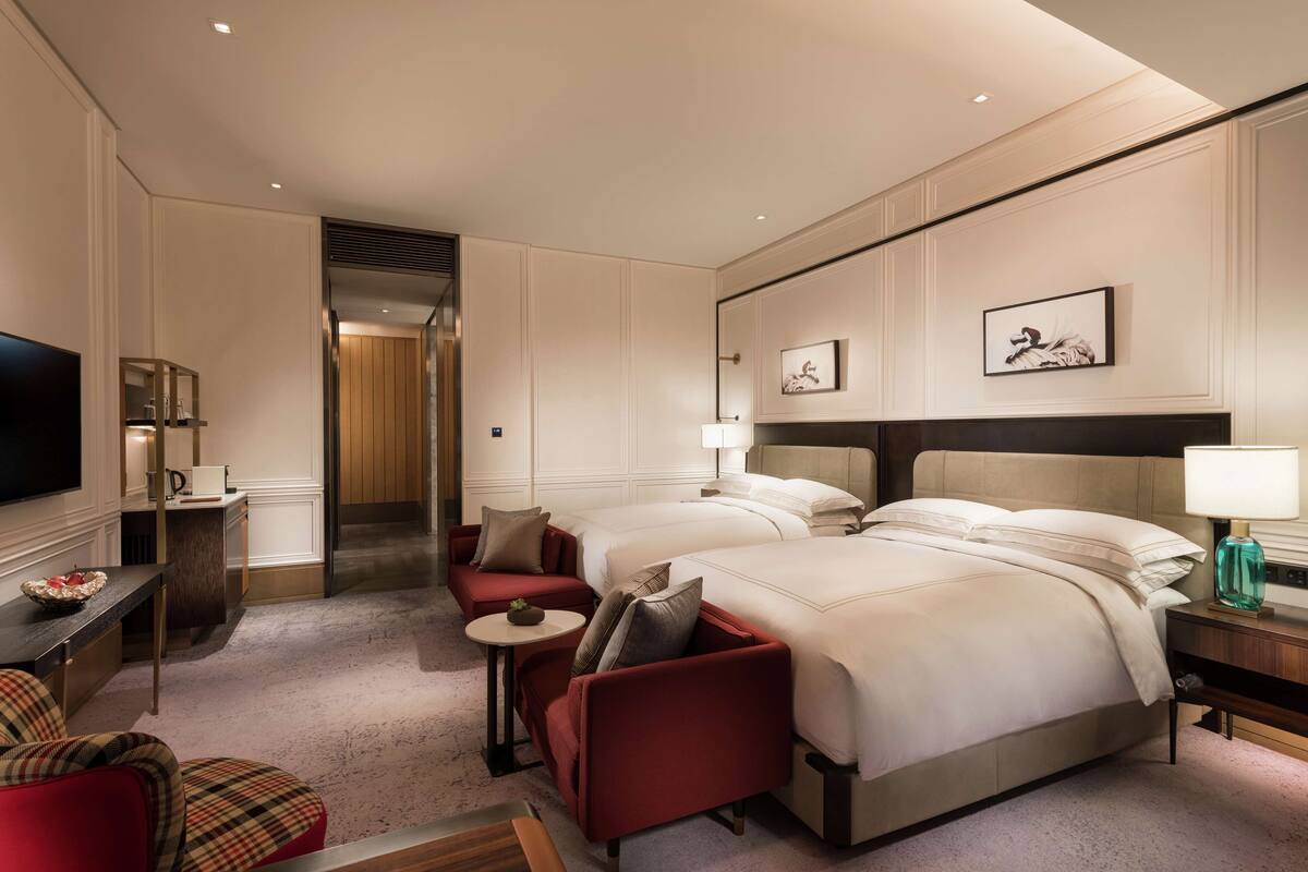 A hotel room with two beds, a TV, a small table, and a seating area with chairs.