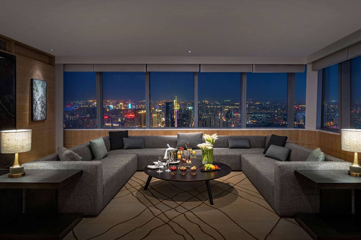 A modern living room with a large sectional sofa, a coffee table with decorative items, and a cityscape view through large windows.