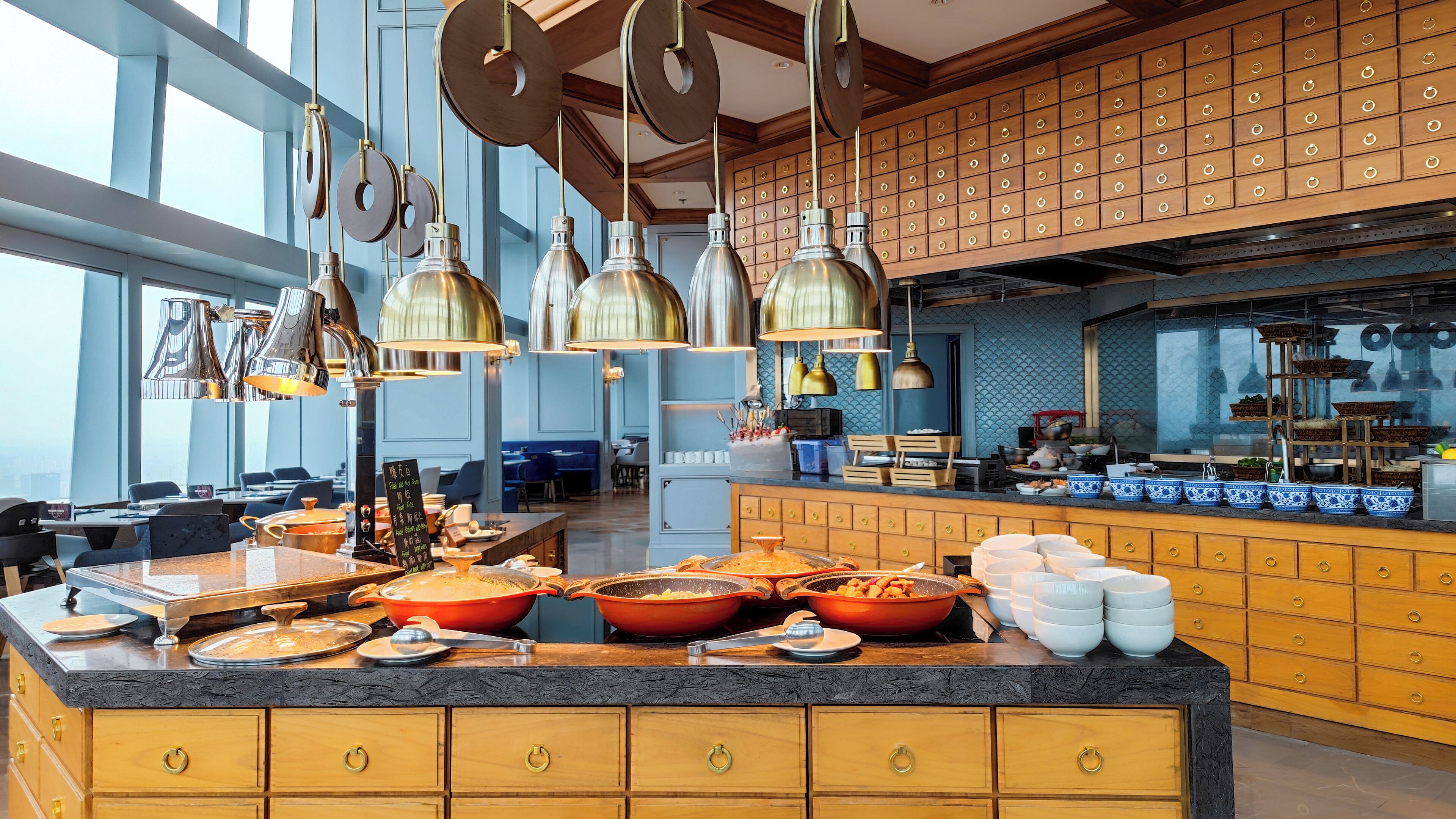 A modern kitchen with a large island, hanging pendant lights, and wooden cabinets.