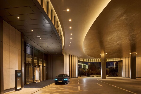 A modern building entrance with a curved ceiling, a car parked in front, and a sign indicating a hotel. - Conrad Shenyang (Shenyang)