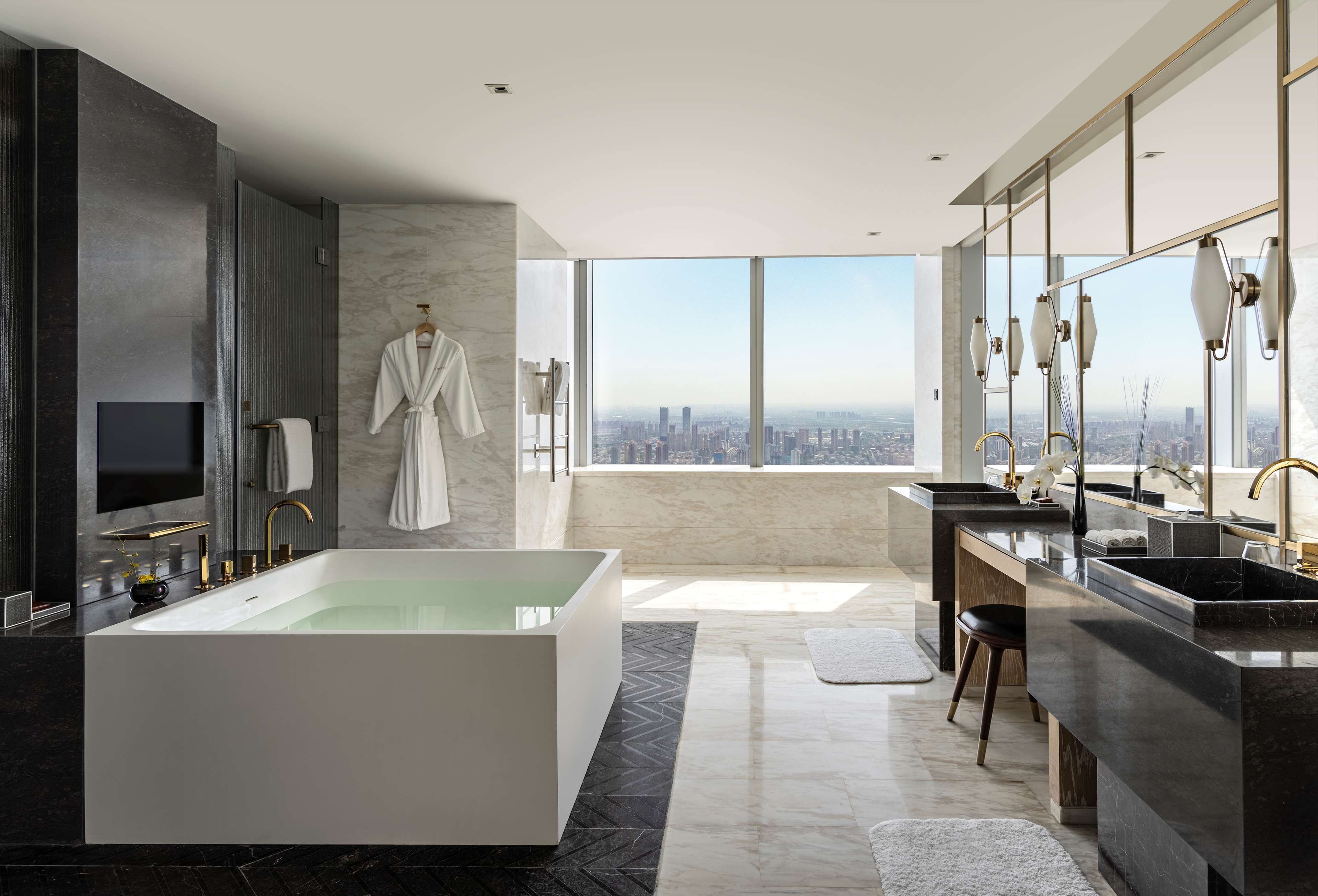 A modern bathroom with a large bathtub, a vanity with a sink, and a large window offering a city view.