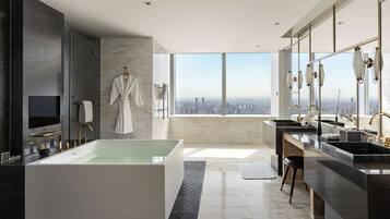 A modern bathroom with a large bathtub, a vanity with a sink, and a large window offering a city view.