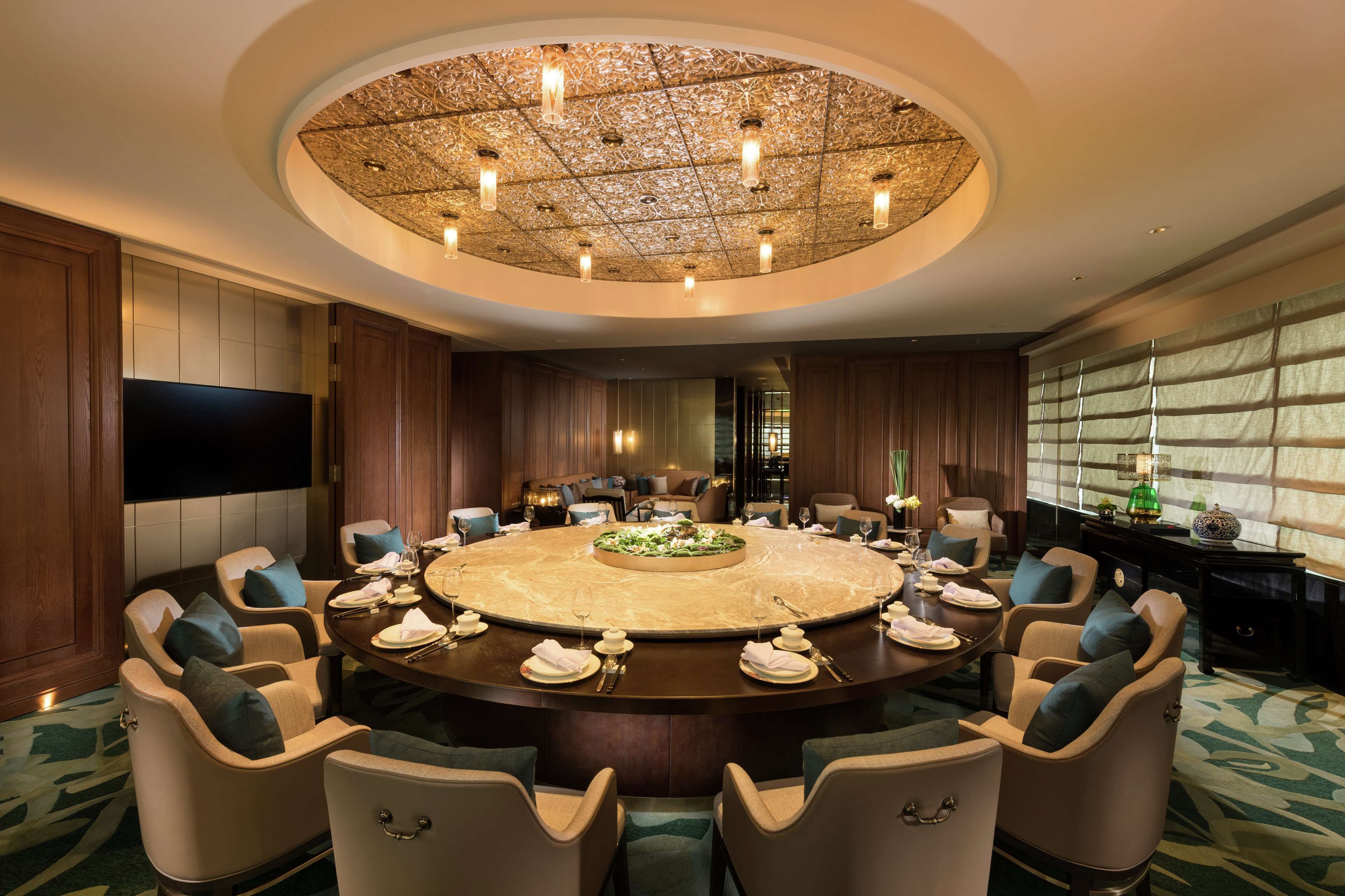 A conference room with a round table, multiple chairs, a large screen, and a decorative ceiling.