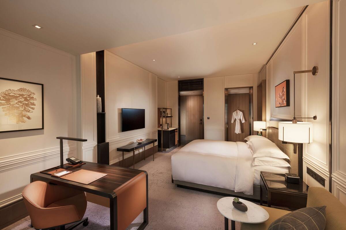 A hotel room with a bed, desk, chair, TV, and a bathroom visible through an open door.