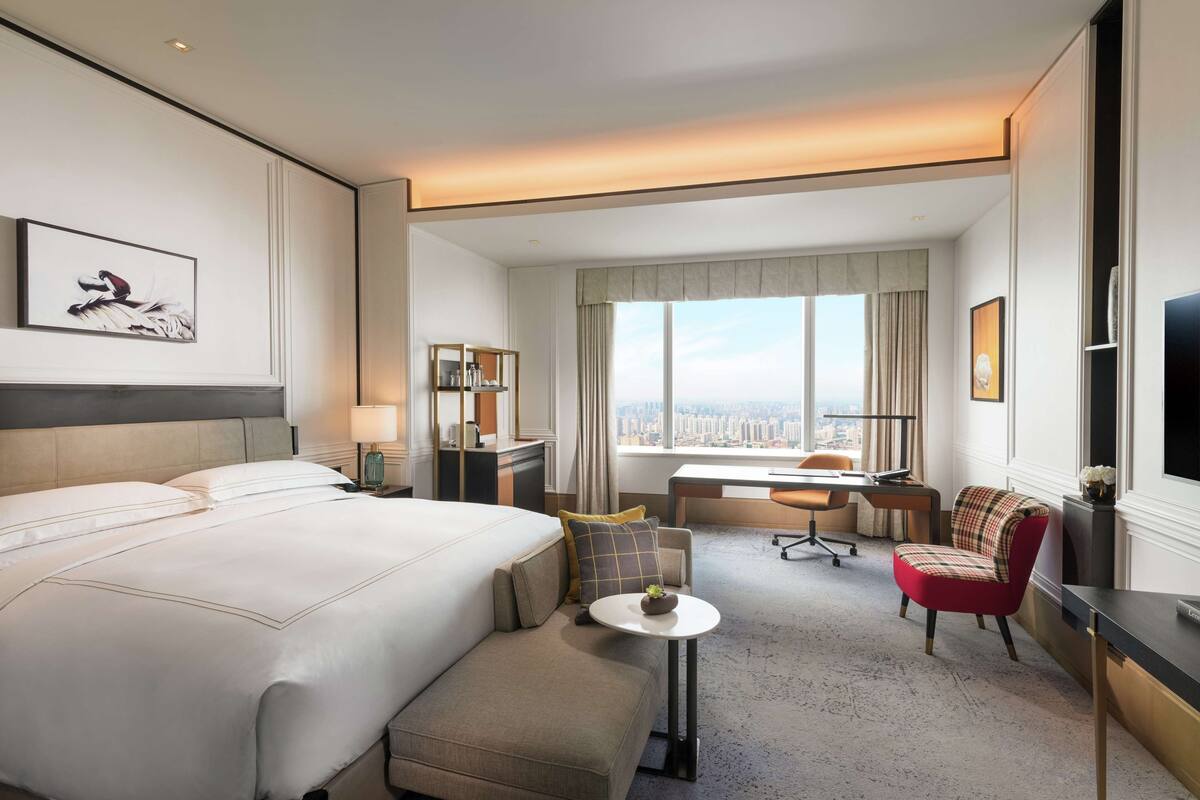 A hotel room with a large bed, a desk, a chair, a small table, and a TV.